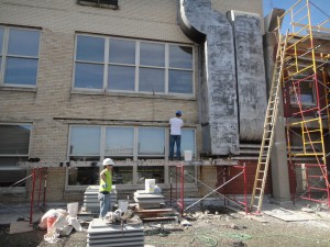 Two masonry contractors restoring stone around windows