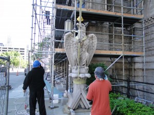 Two masonry contractors guiding a stone sculpture in place